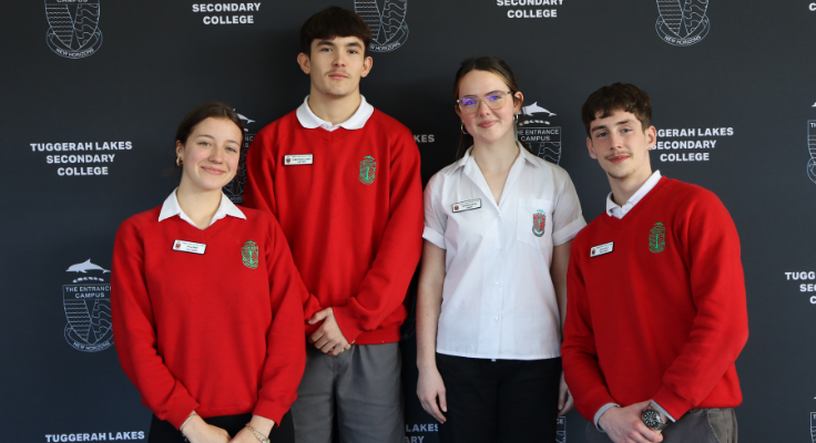a group of 2 male and 2 female students in front of a school backdrop in school uniform