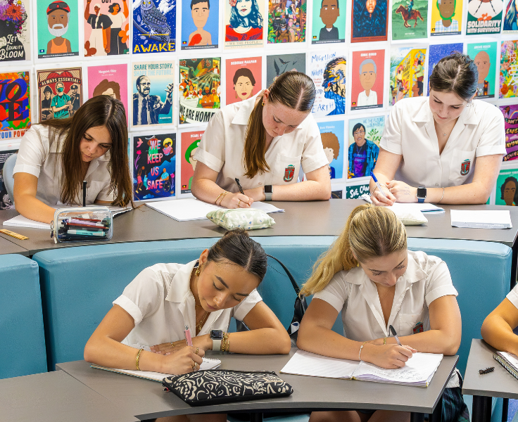 Students writing in booklets in a school library classroom, siting on comfortable furniture
