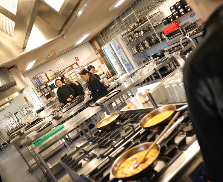 photo of a commercial cooking room with frying pans with food being cooked