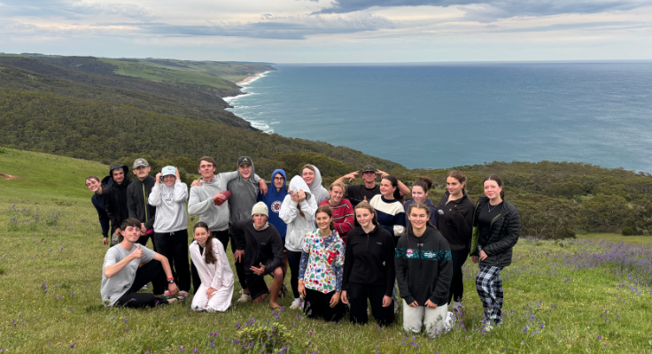 a group of students with a backdrop of the coastline of the beach on the top of a hill