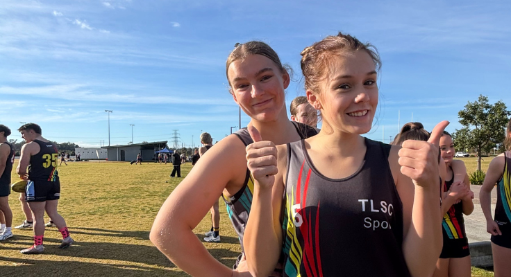 2 students giving a thumbs up in front of an athletics field