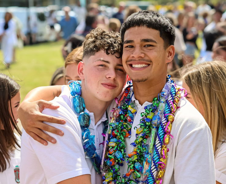 Students embracing with graduation sashes around neck