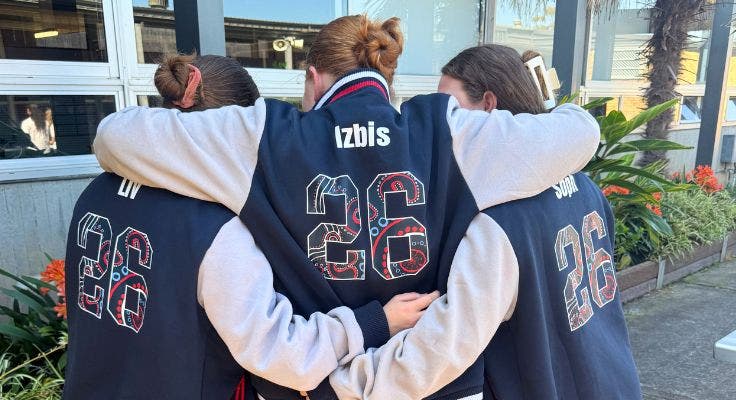 3 students wearing the school jacket facing towards the camera hugging