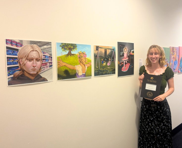 a student holding an award next to 4 canvas paintings