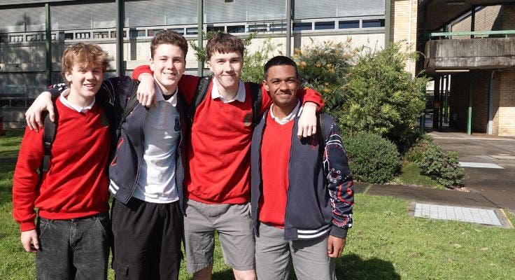 Four male students smiling in front of the school building