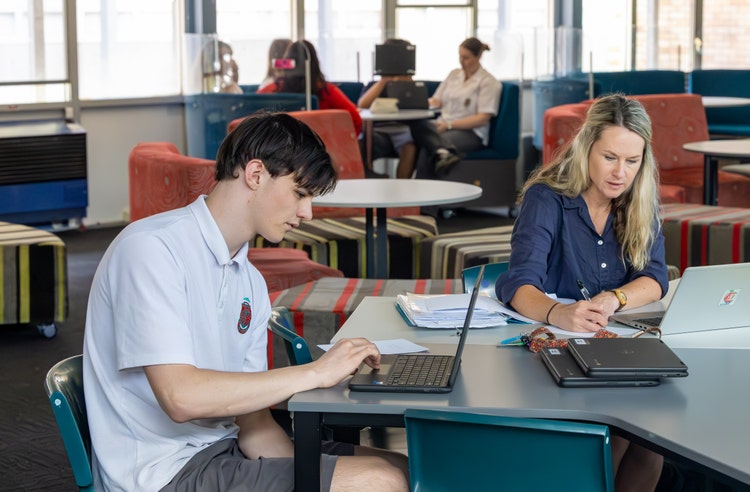 A student and teacher working on laptops in the school library