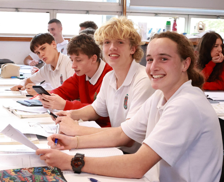 a group of students sitting at a desk in a classroom with papers and calculators out